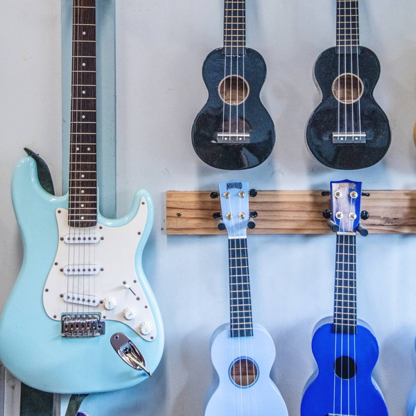 A wall of ukeleles in black, dark blue and light blue and a light blue electric guitar hanging on the wall as well