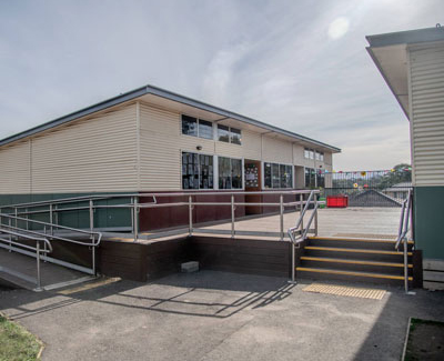 A set of 4 buildings with large windows, featuring a ramp and stairs with a yellow safety strip.