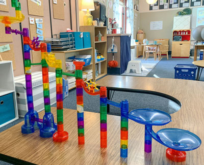 An intricate marble run with colorful, interlocking pieces stands on a classroom table, creating a playful and creative atmosphere.
